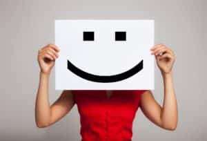 Image of a person holding a piece of paper with a smiley face on it in front of their own face