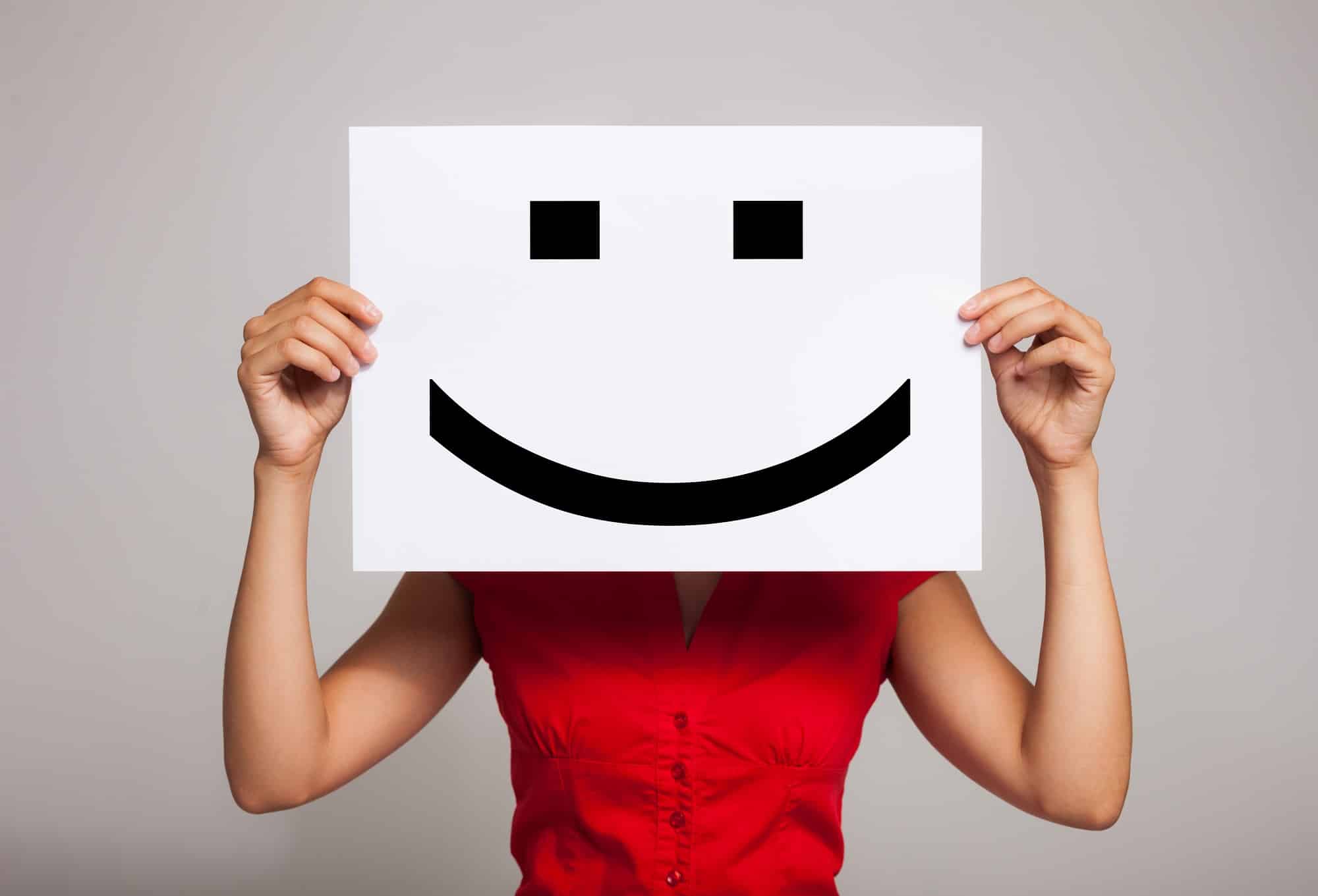Image of a person holding a piece of paper with a smiley face on it in front of their own face