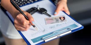 Woman signing a sign in sheet with her keys and ID card on the clip board on PSA Insurance & Financial Services' website