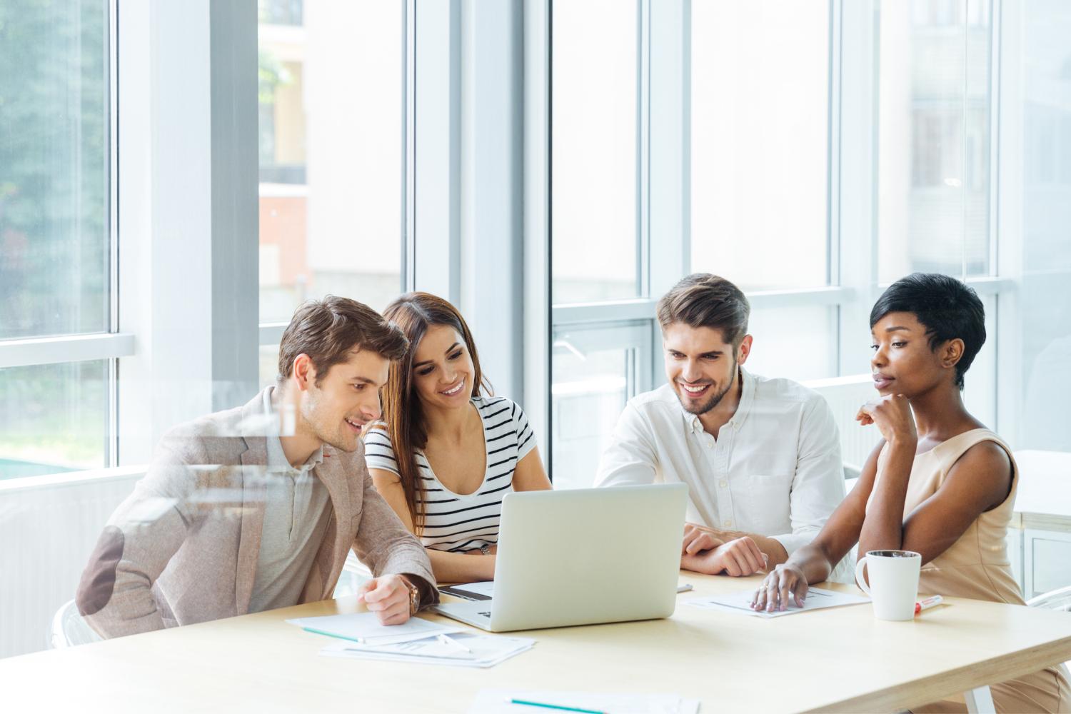 Image of a group of happy employees sitting at a desk looking at a laptop