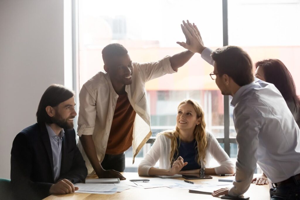 Image of workers high-fiving over a desk with other smiling employees