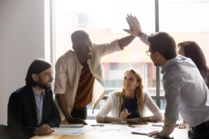 Image of workers high-fiving over a desk with other smiling employees